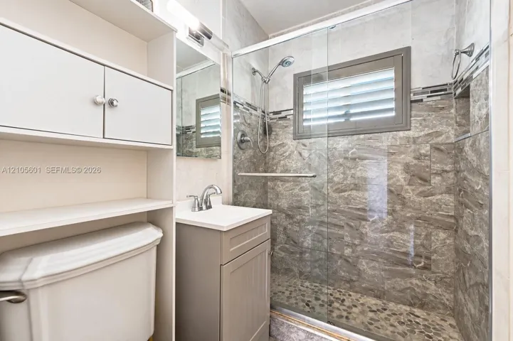 Glass-enclosed shower with pebble-finish flooring and stone-look tile surround