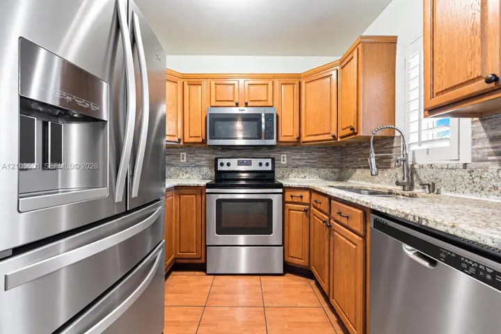 Stainless steel appliances, wood cabinetry, granite countertops, tile flooring, and a tile backsplash