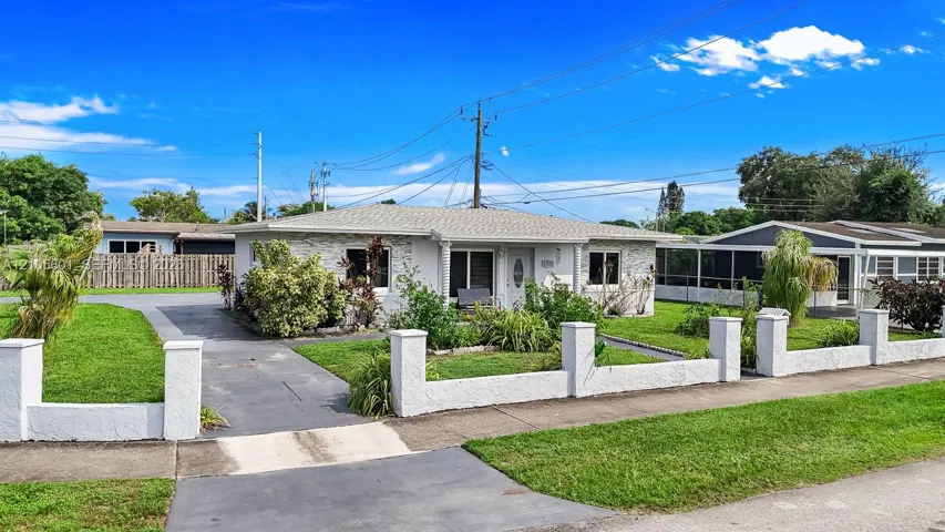 White stucco exterior with a gray shingle roof, complemented by a front yard with green grass and a paved driveway