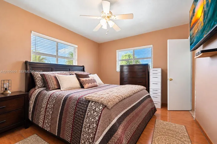 Wood-finish flooring, ceiling fan with light fixture, window with blinds, and a built-in wall shelf
