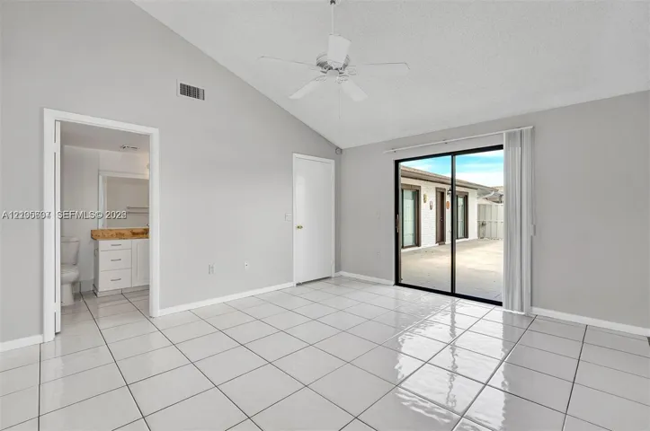Vaulted ceiling with a ceiling fan, white tile flooring, and sliding glass doors leading to a paved outdoor area