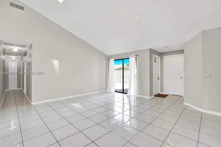 Vaulted ceiling, white tile flooring, sliding glass door, recessed lighting, and a hallway with overhead lighting