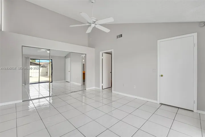 Vaulted ceiling, white tile flooring, ceiling fan, mirrored closet doors, and sliding glass door