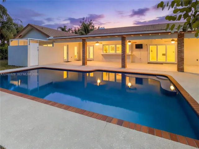 Spacious outdoor pool area featuring a built-in pool, expansive concrete patio, covered patio with brick columns, and a built-in outdoor bar