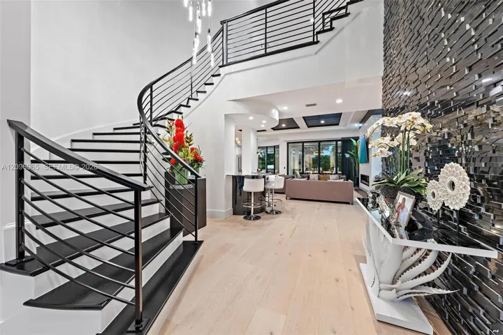 Grand foyer featuring a curved staircase with black metal railings, light wood-finish flooring, a textured black stone accent wall, and recessed ceiling lighting