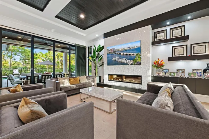 Coffered ceiling with dark wood-finish paneling, floor-to-ceiling glass sliding doors, horizontal linear fireplace, textured stone-surround accent wall, and built-in wall shelving