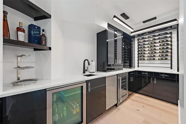 Wet bar featuring high-gloss black cabinetry, white countertops, a built-in wine refrigerator, custom wall-mounted wine racking, and linear LED lighting