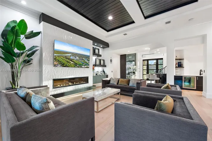 Coffered ceiling with dark wood finish, linear gas fireplace, textured wall surround, recessed lighting, and integrated wet bar