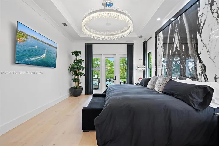 Tray ceiling with a circular crystal chandelier, large-format stone accent wall, and wood-finish flooring