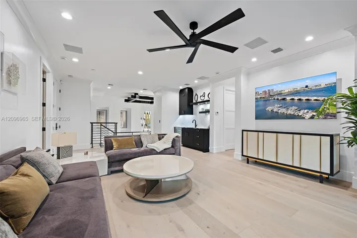 Open-concept space featuring light wood-finish flooring, recessed lighting, matte black multi-blade ceiling fan, and built-in wet bar with dark cabinetry
