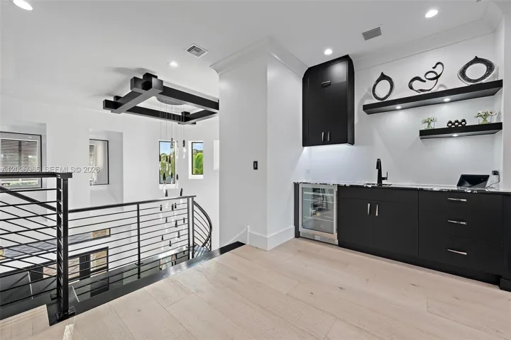 Wet bar featuring matte black cabinetry, stone countertops, integrated under-counter refrigeration, and floating display shelving