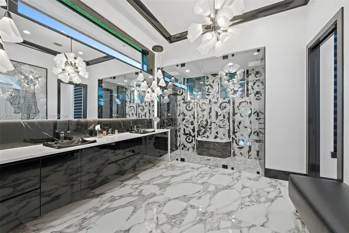 Bathroom featuring high-gloss black cabinetry, white stone-finish countertop, dual integrated sinks, glass-enclosed shower with patterned tile, and large-format tile flooring