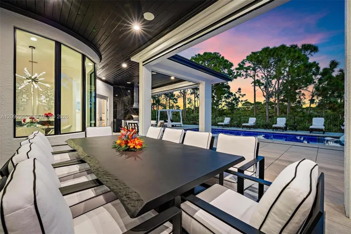 Covered outdoor living space featuring a dark wood-paneled ceiling, recessed lighting, and large-format paver decking with a swimming pool