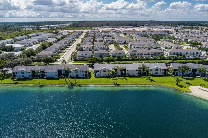 Aerial perspective of residential structures featuring waterfront positioning, expansive green lawns, mature palm trees, and multi-unit composition