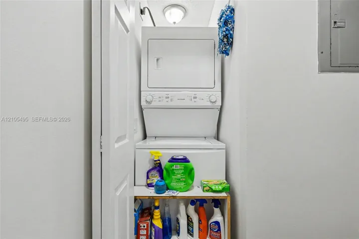 Stacked laundry unit featuring white enamel finish, ceiling-mounted light fixture, and dedicated closet space with bi-fold door