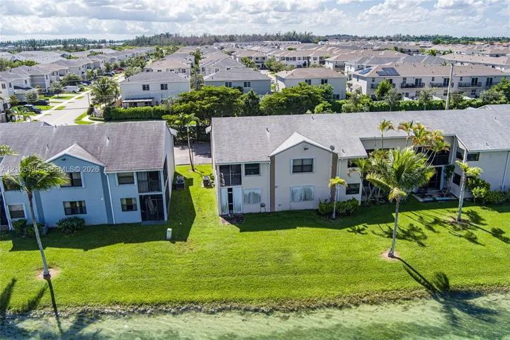 Multi-family residential buildings featuring pitched shingle roofs, screen-enclosed lanais, and a waterfront grass lawn with mature palm trees