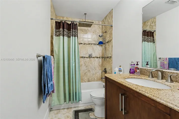 Bathroom featuring a dark wood-finish vanity with a stone countertop, an integrated oval sink, a shower-tub combination with stone-tile surround, and a rainfall showerhead