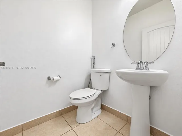Bathroom featuring a white pedestal sink, polished chrome faucet, oval wall-mounted mirror, and tile flooring