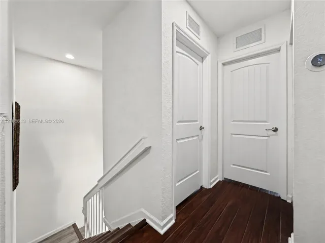 Hallway featuring wood-finish flooring, two solid-core arched two-panel doors, and a smart thermostat