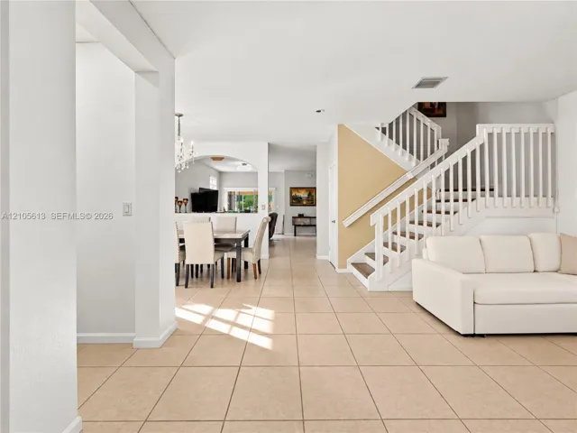 Ceramic tile flooring throughout the open floor plan, staircase featuring white wooden balusters, and arched entryway