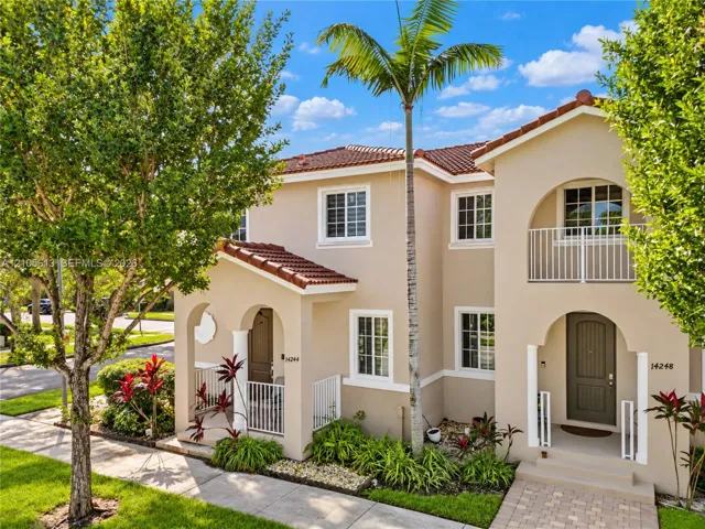Stucco exterior featuring dual-arched entryways, a tiled roof, white metal railings, and a second-story balcony