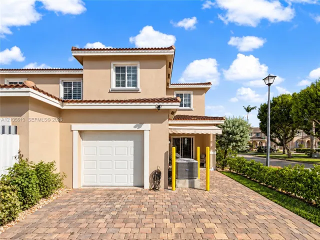 Stucco exterior with multi-level roofline, clay-tile roofing, attached garage, and paved stone driveway