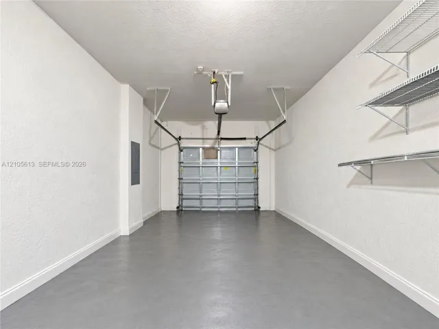Garage space featuring a smooth painted floor finish, textured walls, overhead door opener, and mounted wire shelving units