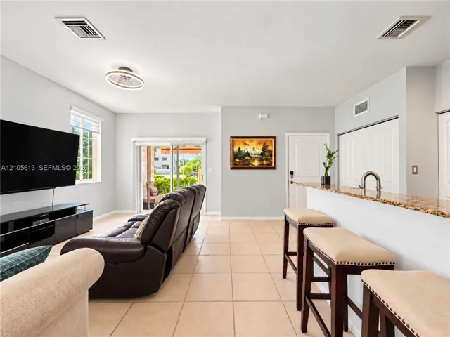 Open-concept interior featuring light-toned tile flooring, a stone-surfaced breakfast bar with a metallic faucet, sliding glass doors, and a modern circular flush-mount light fixture
