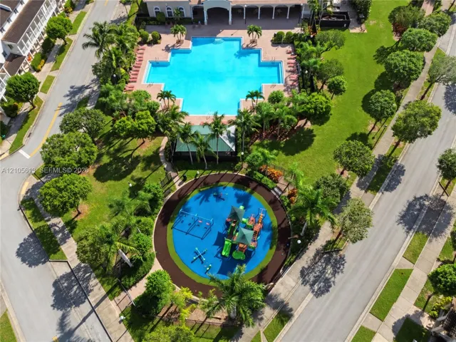 Aerial perspective featuring a communal swimming pool, a playground with specialized rubberized surfacing, paved walking paths, and mature landscaping