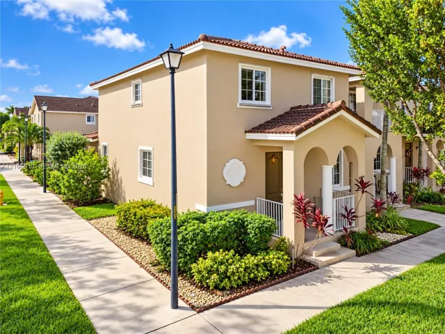 Stucco exterior featuring a covered entryway with arched openings, tiled roof, white-trimmed windows, and decorative architectural medallion