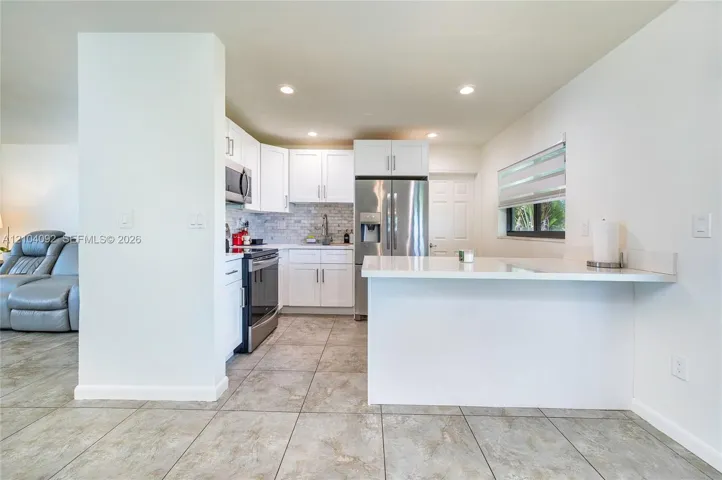 Kitchen featuring white shaker-style cabinetry, quartz countertops, stainless steel appliances, tiled backsplash, and stone-finish tile flooring