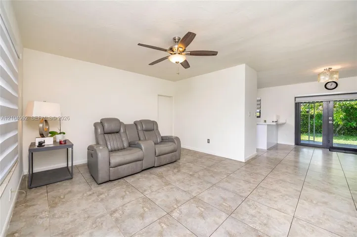 Neutral tile flooring, ceiling fan with light kit, and double glass sliding doors leading to the exterior