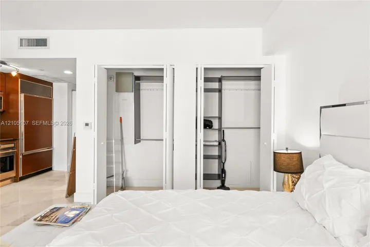 Two built-in closets with bi-fold doors, recessed lighting, and a white upholstered headboard