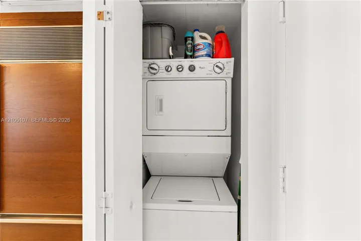 Stackable washer and dryer unit within a built-in closet, featuring white panel doors