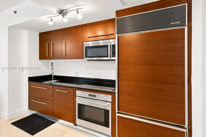 Sleek kitchen with wood-finish cabinetry, stainless steel appliances, black countertops, and a built-in oven
