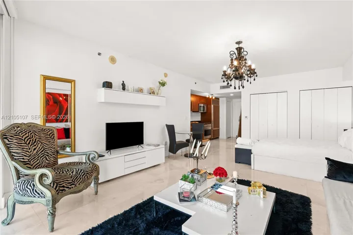 Open-concept living space with light-toned flooring, featuring a kitchen area, built-in storage closets, and a decorative chandelier