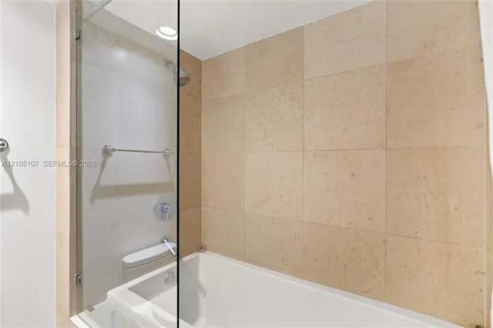 Built-in bathtub with glass shower enclosure, beige tiled walls, recessed lighting, and chrome fixtures