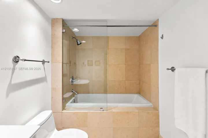 Bathtub with glass shower enclosure, full height tiled surround, and polished chrome fixtures