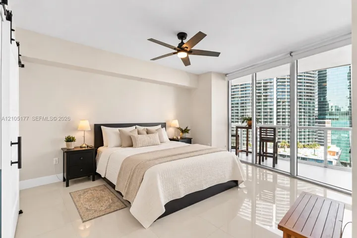 Floor-to-ceiling glass windows, polished tile flooring, sliding barn door, and a multi-blade ceiling fan with integrated lighting