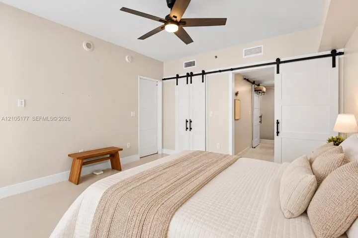 Neutral wall palette featuring white barn-style sliding doors with matte black hardware, recessed ceiling lighting, and a dark-finish ceiling fan