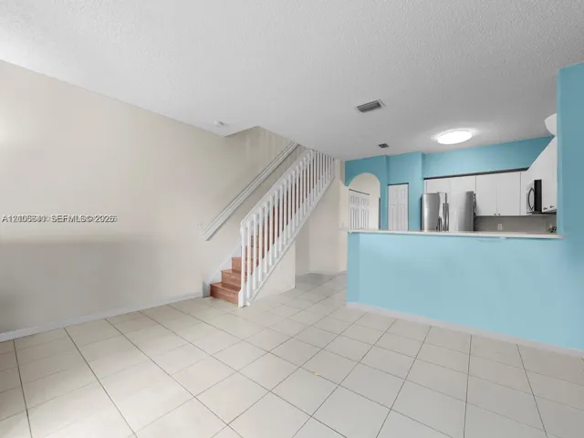 Open-concept floor plan with tile flooring, white cabinetry, built-in breakfast bar, and staircase featuring a painted wood balustrade