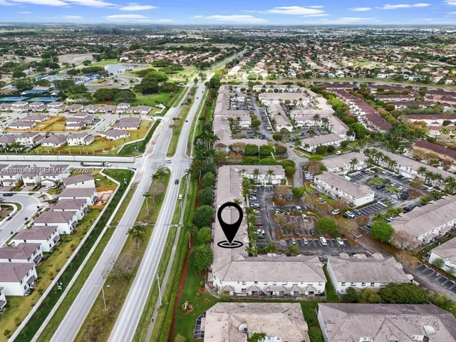 Aerial perspective featuring residential multi-unit structures, integrated paved surface parking, mature landscaping, and multi-lane thoroughfares