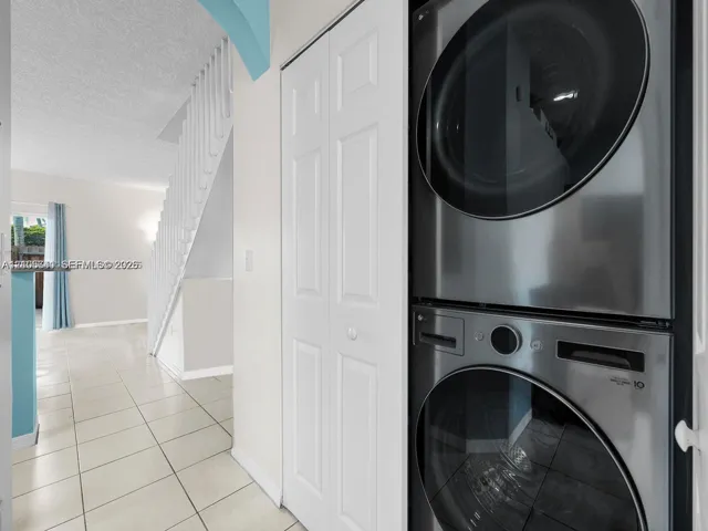 Stacked stainless steel laundry appliances, ceramic tile flooring, and white louvered closet doors