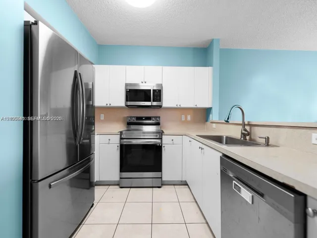 Kitchen featuring white cabinetry, stainless steel appliances, neutral solid-surface countertops, a stainless steel undermount sink with a gooseneck faucet, and tile flooring