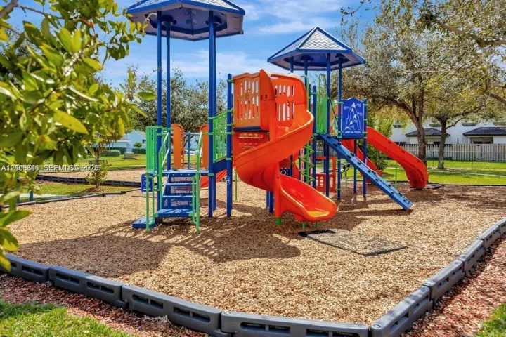 Outdoor playground structure featuring spiral slides, climbing apparatus, and modular platforms, contained within a mulched area and bordered by a reinforced landscape barrier