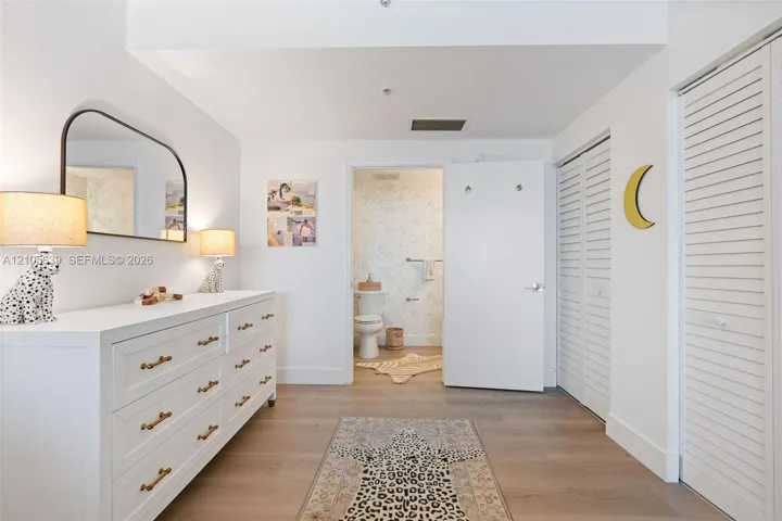 Neutral-toned wood-finish flooring, dual-door louvered closets, and arched wall-mounted mirror