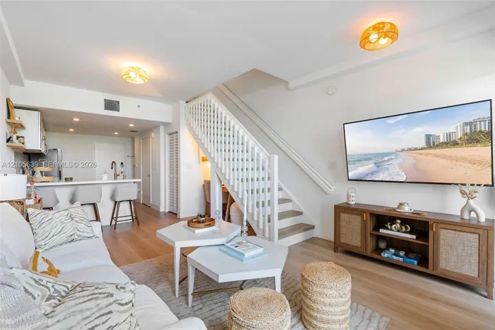 Open-concept living space featuring wood-finish flooring, a white staircase with balusters, built-in kitchen cabinetry, a breakfast bar, and flush-mount lighting fixtures