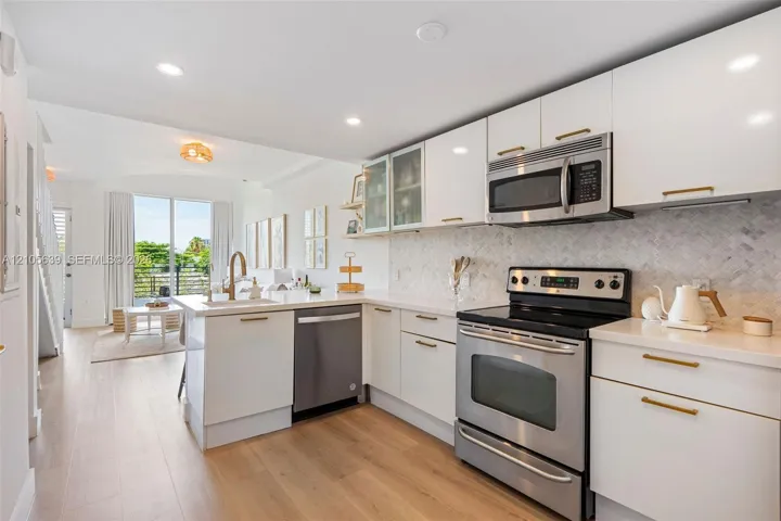 Kitchen featuring white cabinetry with brass hardware, stainless steel appliances, quartz countertops, herringbone-patterned tile backsplash, and wood-finish flooring