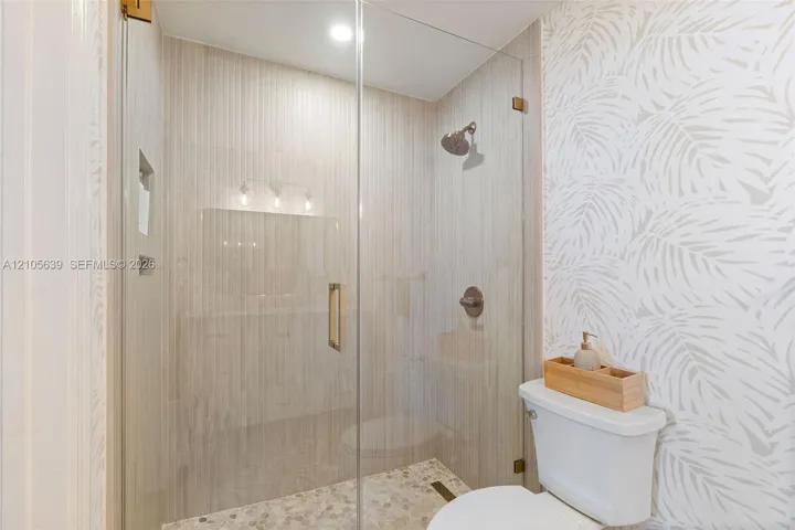 Frameless glass shower enclosure featuring vertical tile surround, recessed wall niche, pebble-texture shower floor, and metal-finish shower fixtures