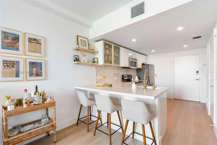 Kitchen featuring white flat-panel cabinetry, quartz countertops, integrated stainless steel appliances, open wood shelving, and wood-finish flooring